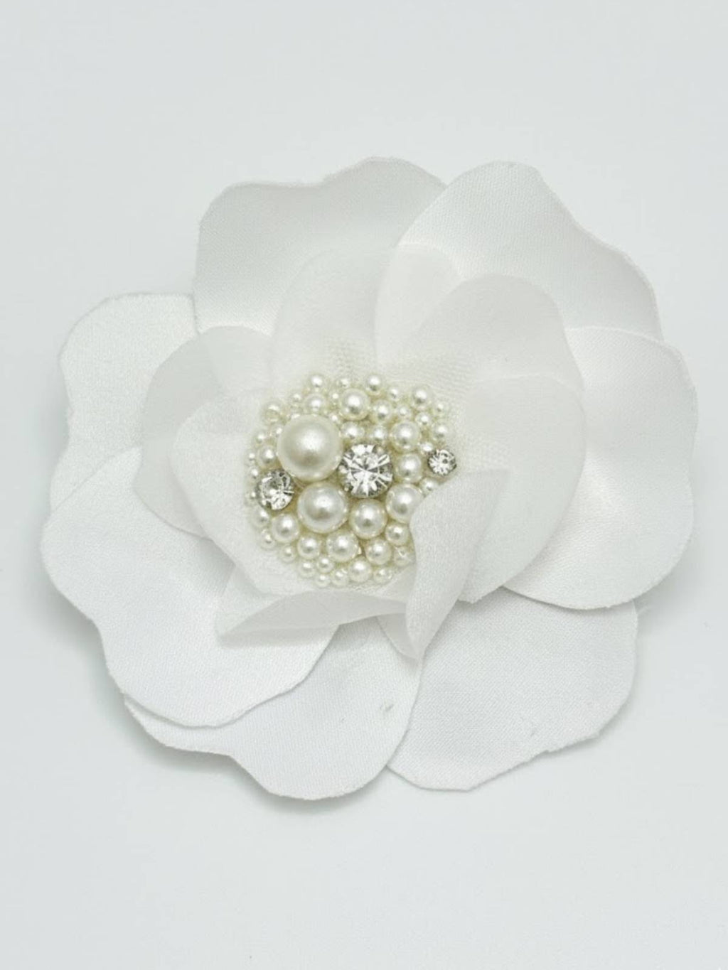 White flower hair clip with pearl and crystal center on a light gray background