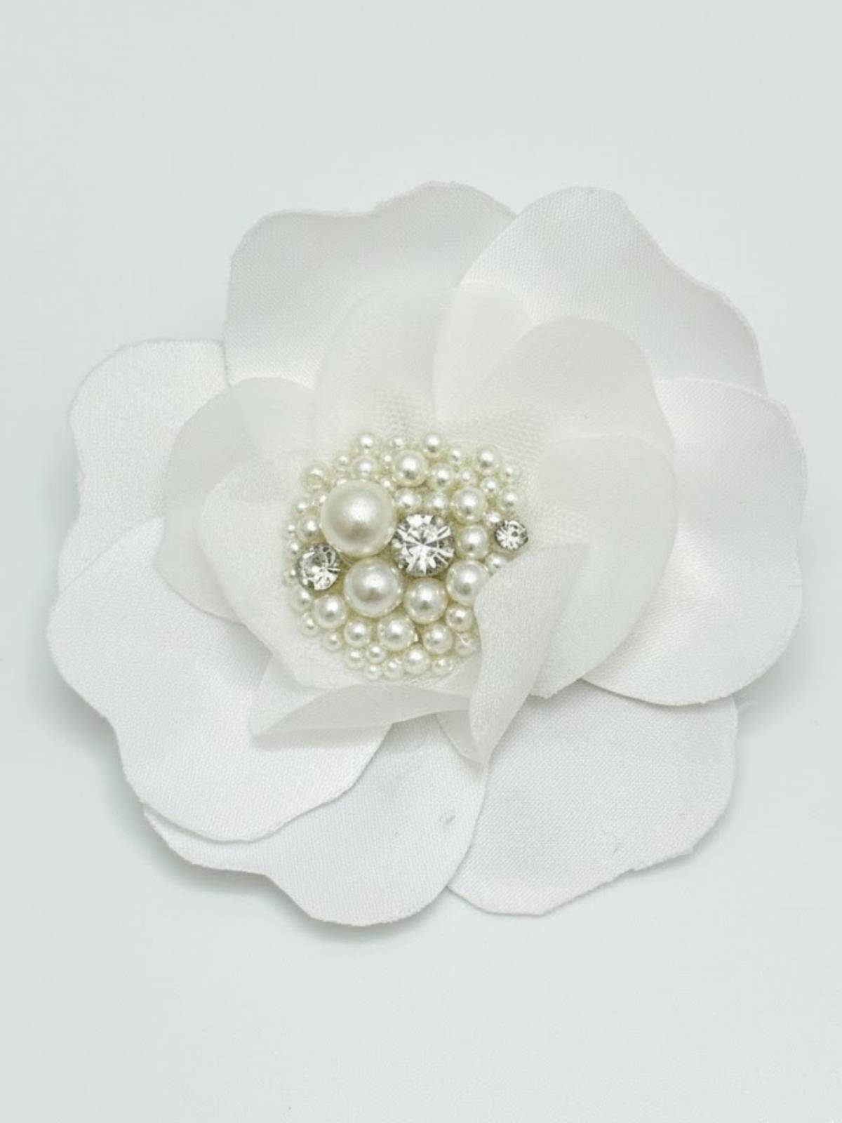 White flower hair clip with pearl and crystal center on a light gray background