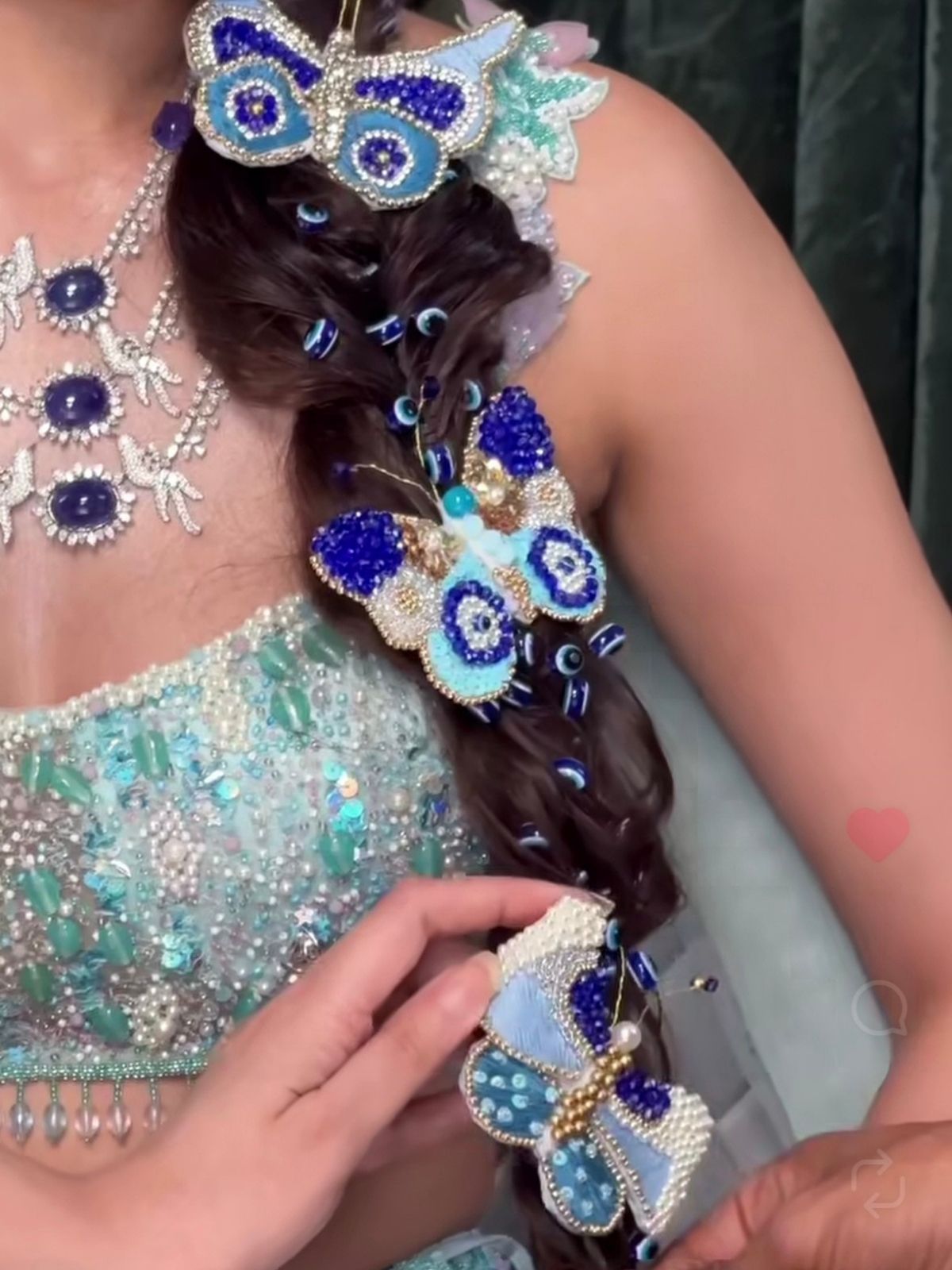 Decorative hair braid with blue and silver butterflies by loveknots and evil eyes held by a person wearing a sparkling outfit.