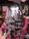 influencer with long wavy hair wearing a feather dream bow, with a blurred indoor setting in the background.