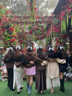 Group of women wearing handmade hair bows, posing outdoors amid lush floral decorations.