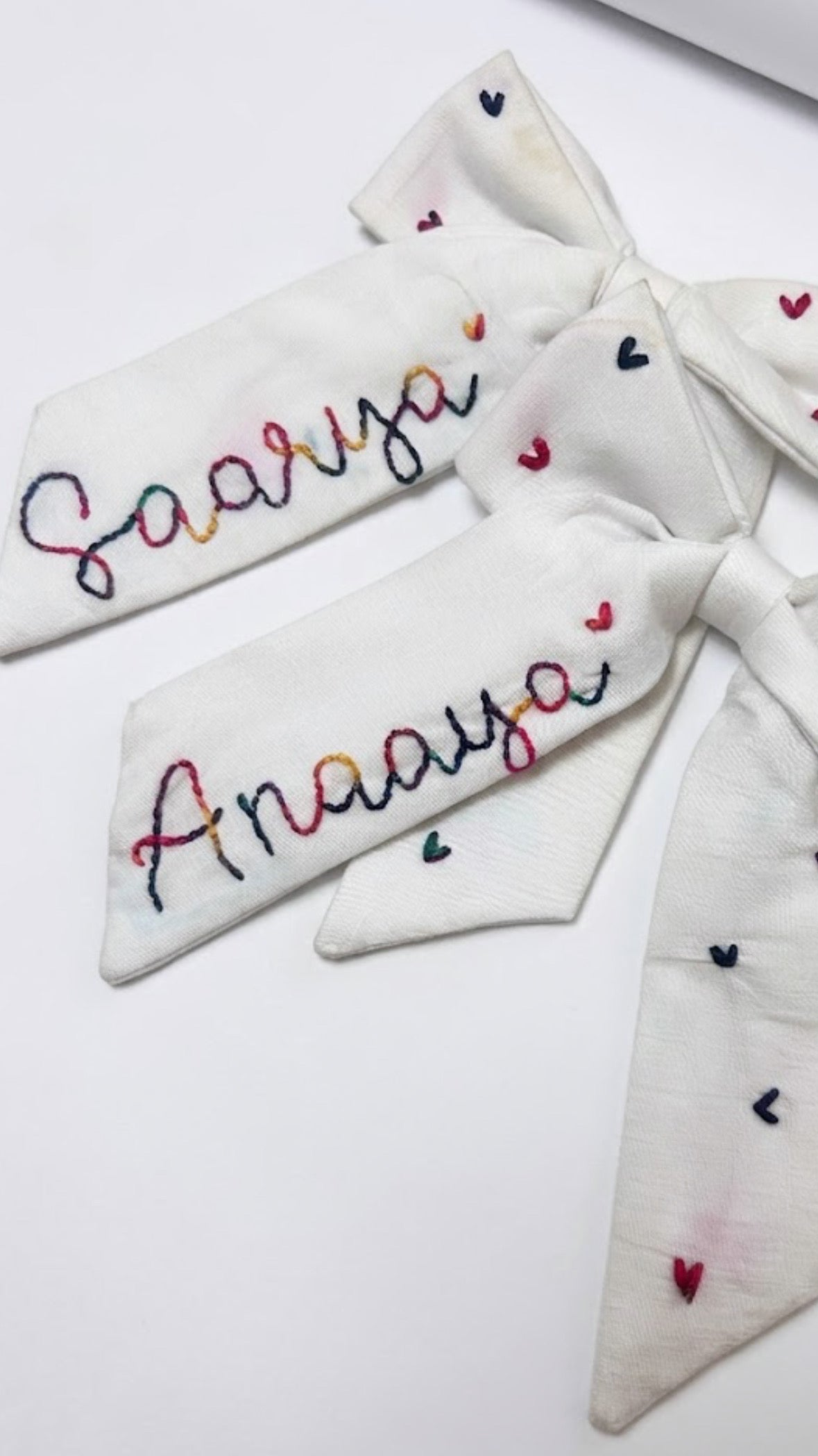 Two white bow with embroidered names on a light background