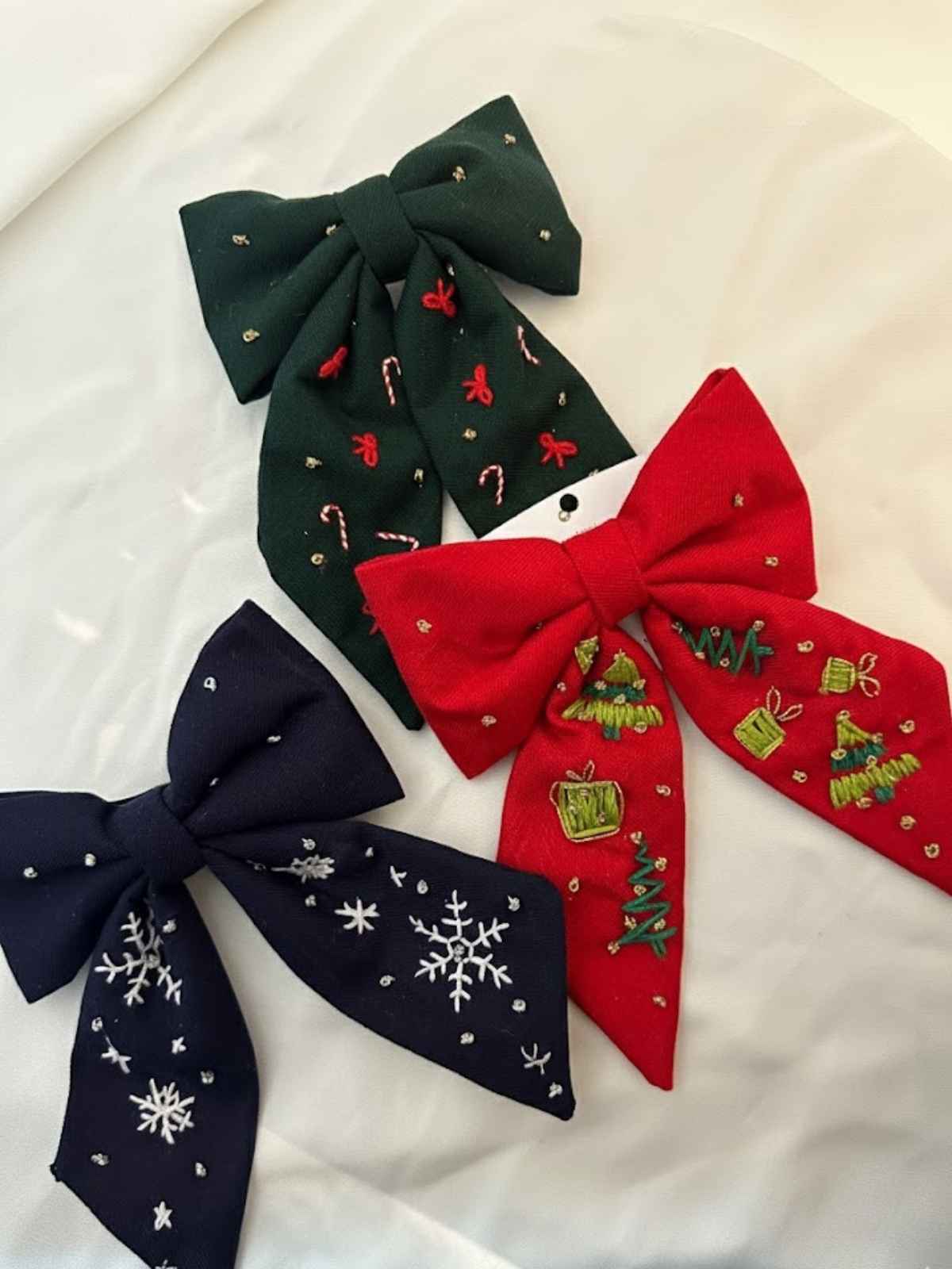 Three hand embroidered pashmina bows in green, red, and navy on a white background