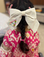 Child with braided hair wearing a large white personalised name hair bow, sitting on a couch.