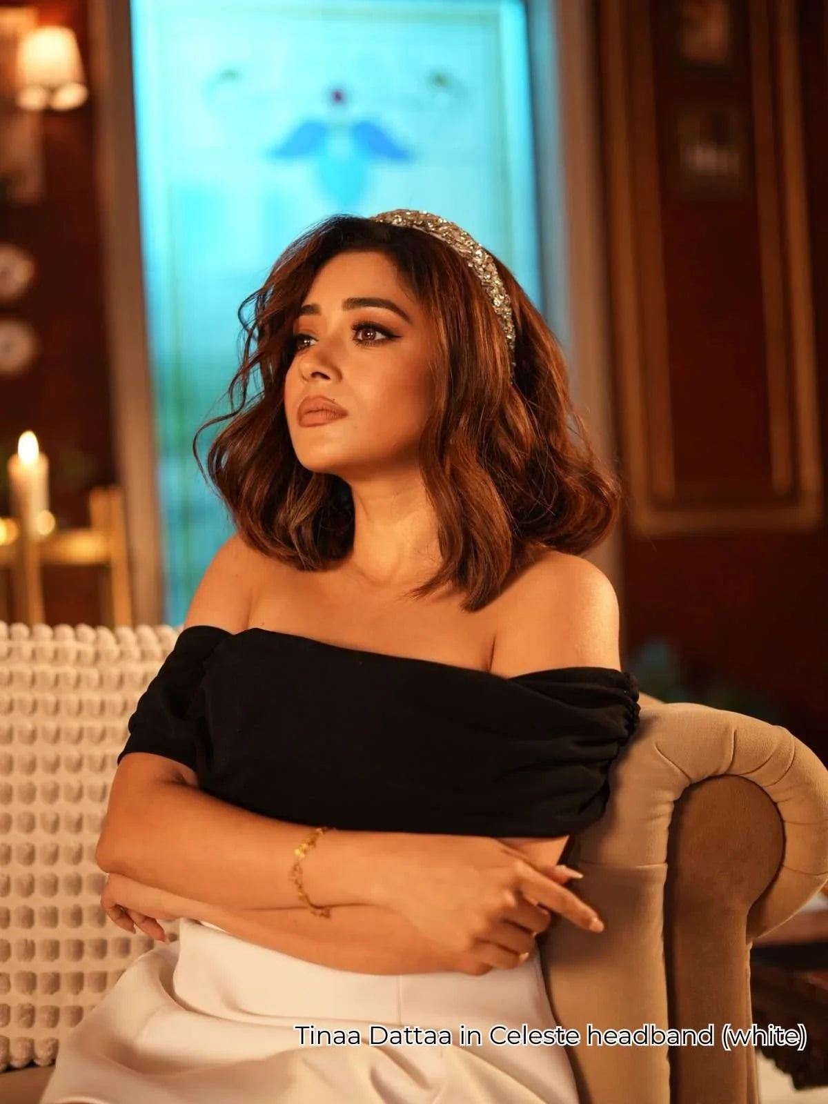 Tinaa Datta wearing a black off-shoulder top with a crystal headband by loveknots, sitting on a couch.