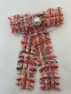 Pink Tweed bow with fringed edgeswith a decorative button on a white background