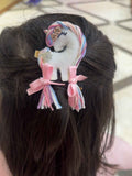 Hair clip with a unicorn design and pink bows on dark hair