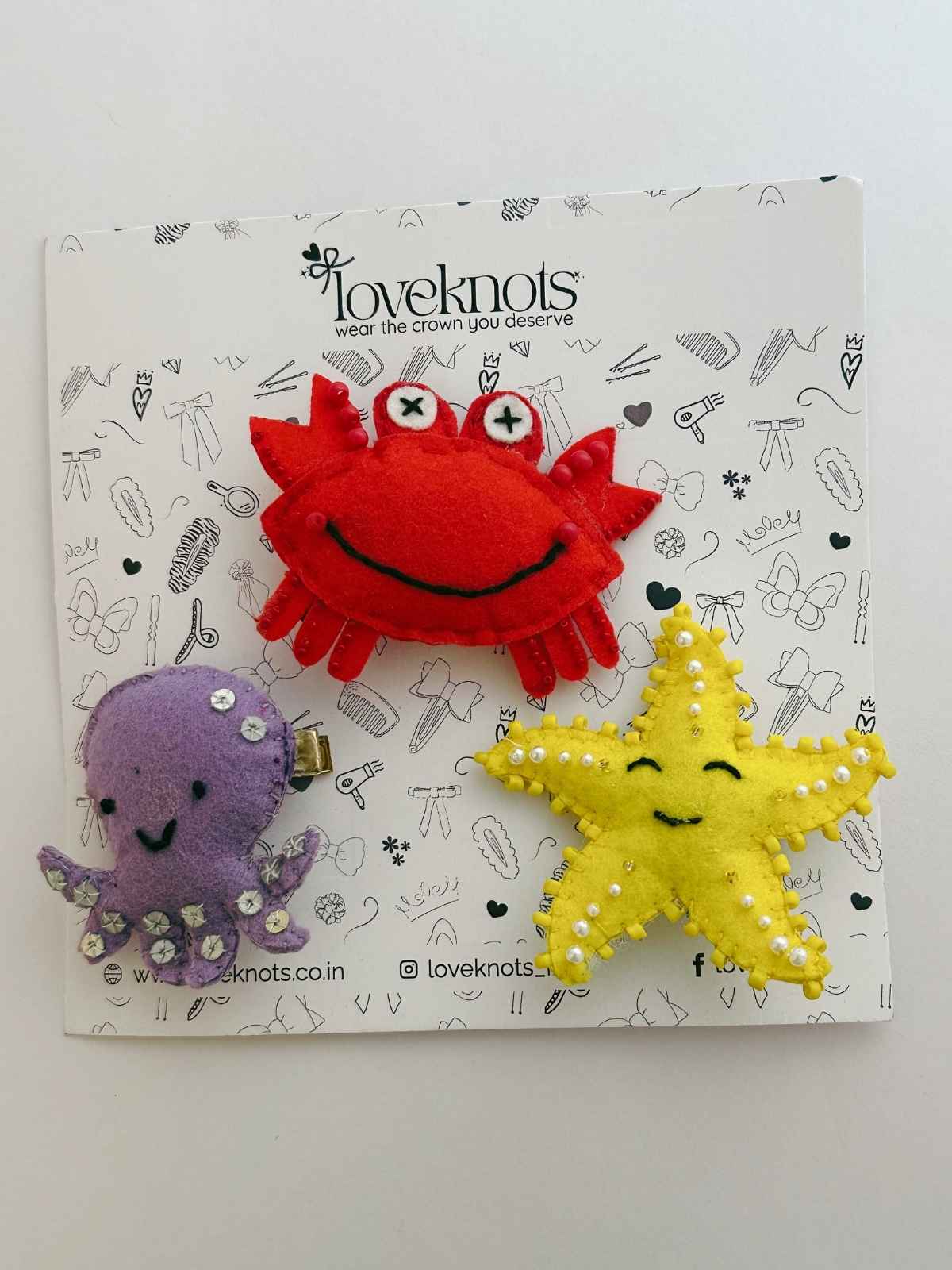 Three colorful hair accessories (crab, octopus, starfish) on a branded loveknots packaging background.