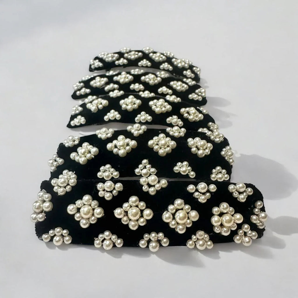 Set of black hair clips with white pearl embellishments on a light gray background