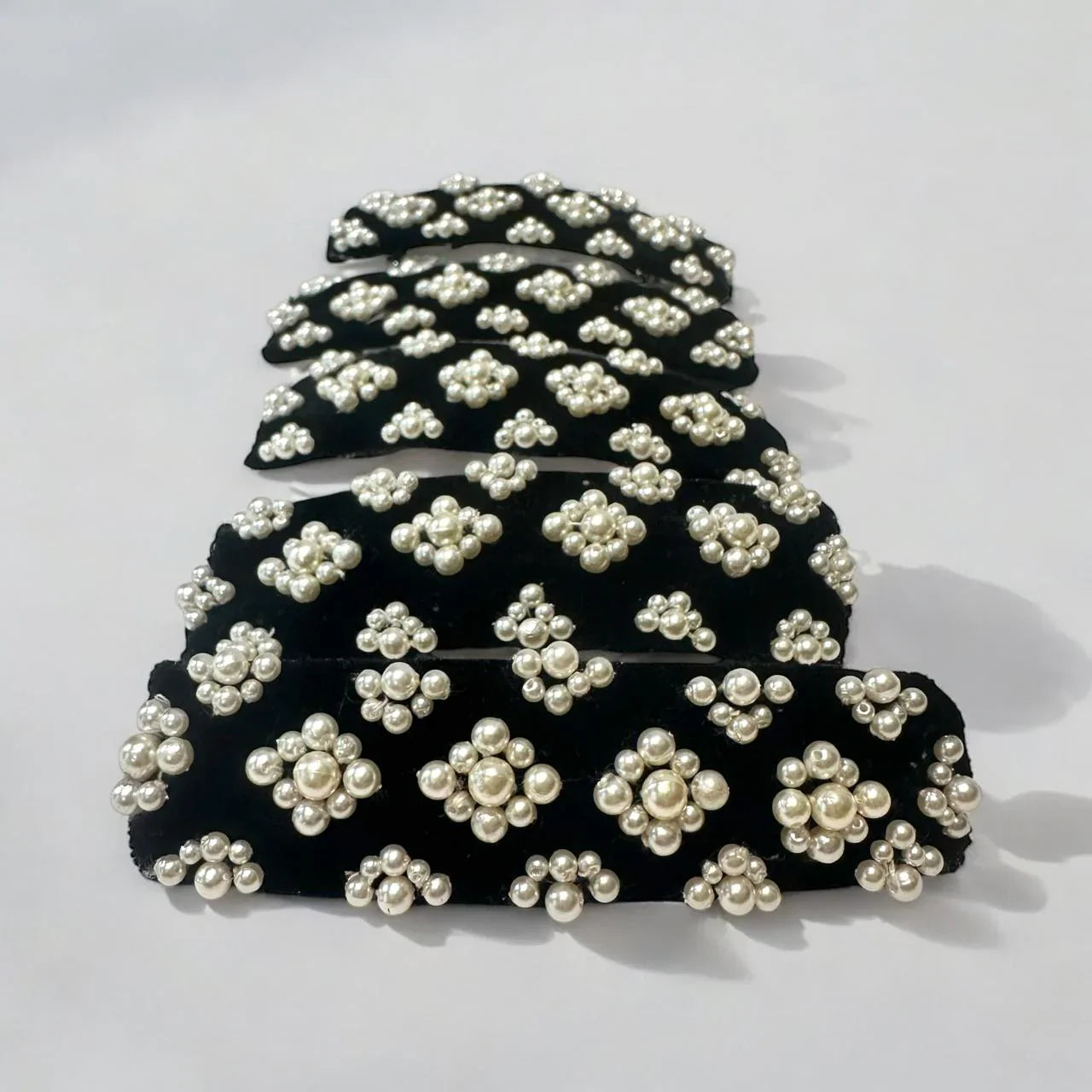 Set of black hair clips with white pearl embellishments on a light gray background
