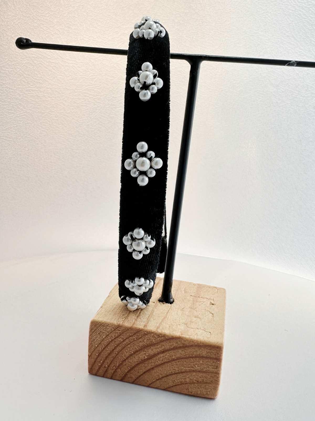 Black hairband with white floral designs on a wooden block stand against a white background