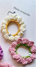 Two handmade crocheted scrunchies on a white background, one cream and yellow and labeled 'Daisy scrunchie', and one pink and green. A partial purple scrunchie is visible at the bottom left.