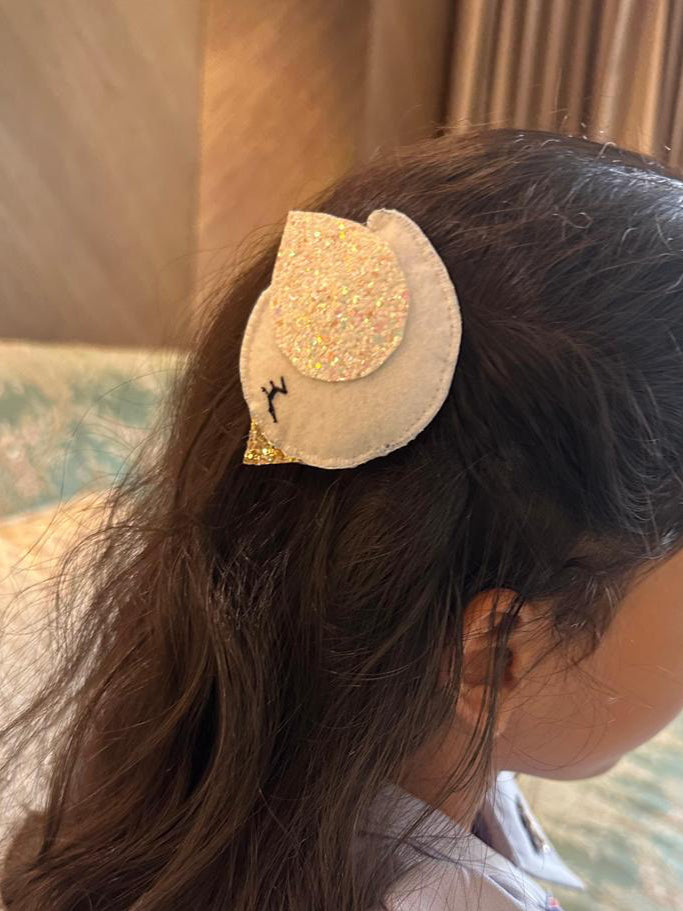 Child with a decorative bird hair clip in a room with curtains and furniture.