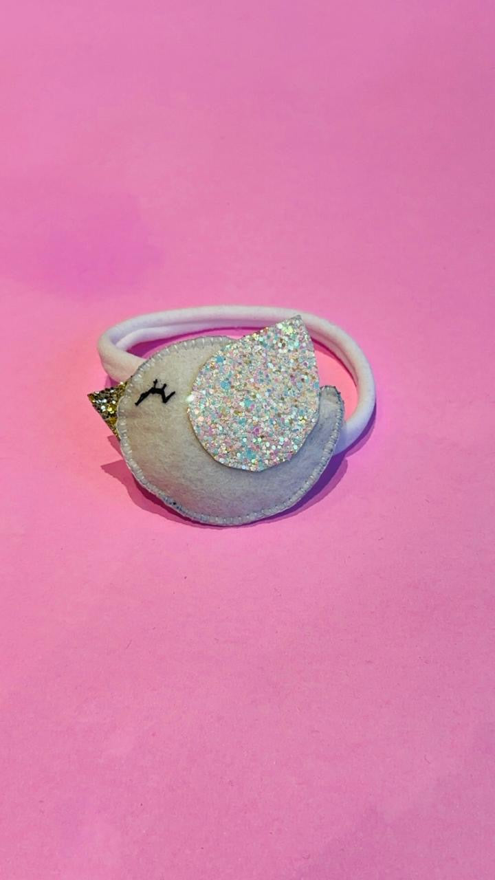 Sparkly bird-shaped clip with baby band on a pink background
