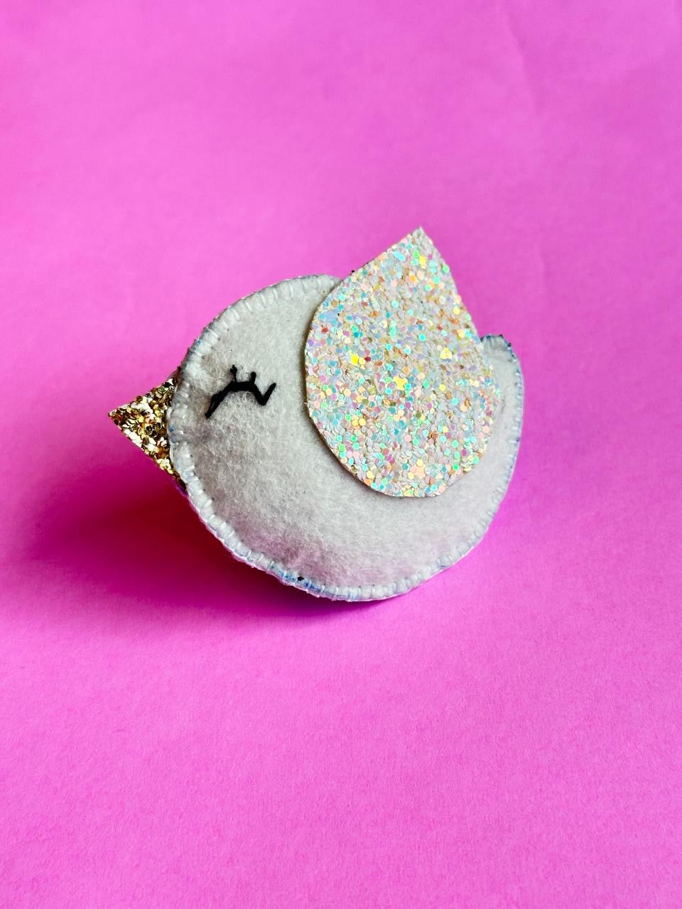 Small plush bird with a glittery wing on a pink background