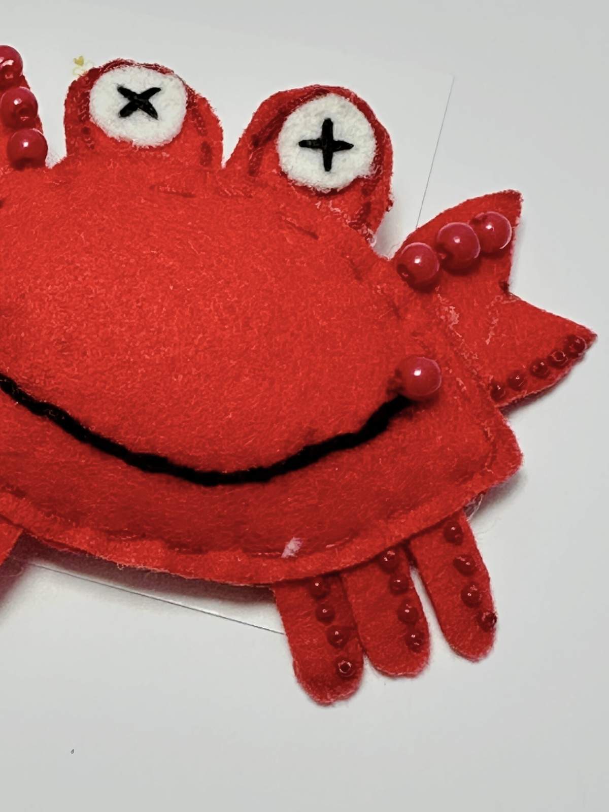 closeup of Red felt crab hair clip with beads details on a white loveknots background