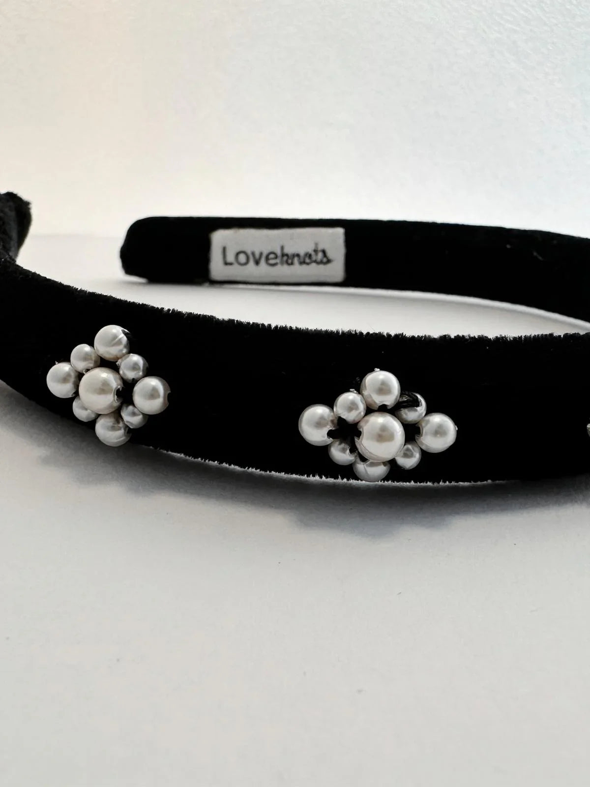 Black headband with white floral pearl embellishments on a white background