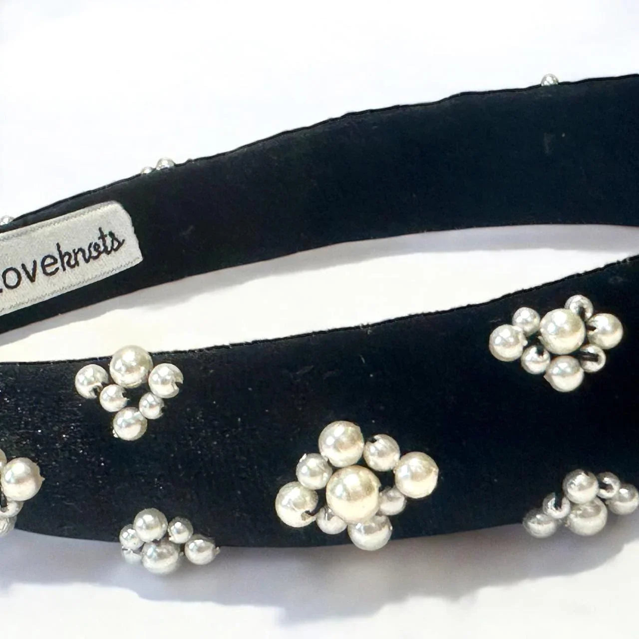 closeup of black velvet hairband with pearl embellishments on a white background