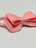 Pink bow hair clip with pearl details on a light gray background