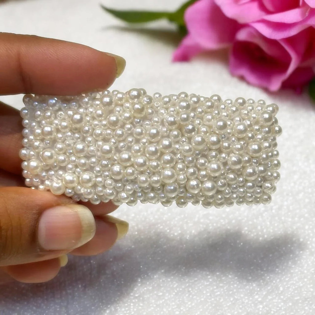 Hand holding a pearl-embellished clip with a pink flower in the background