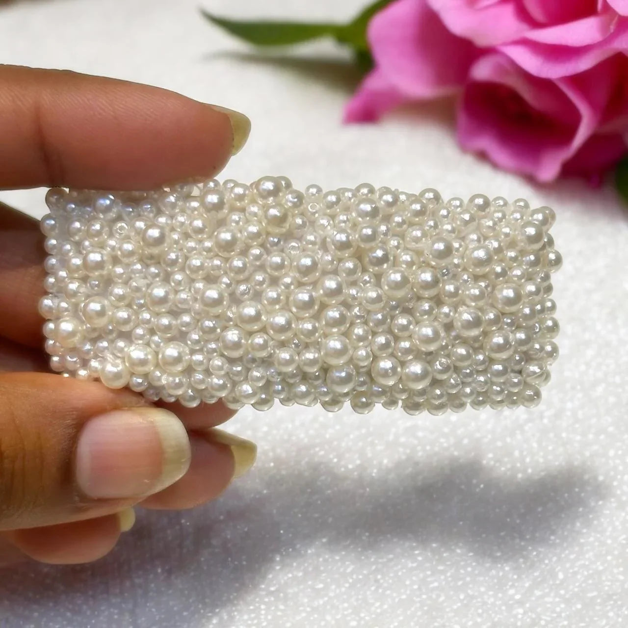 Hand holding a pearl-embellished clip with a pink flower in the background