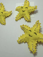 Three yellow star-shaped hair clips with pearl embellishments on a loveknots white background