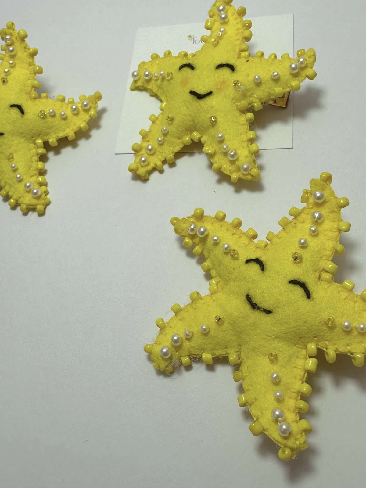 Three yellow star-shaped hair clips with pearl embellishments on a loveknots white background