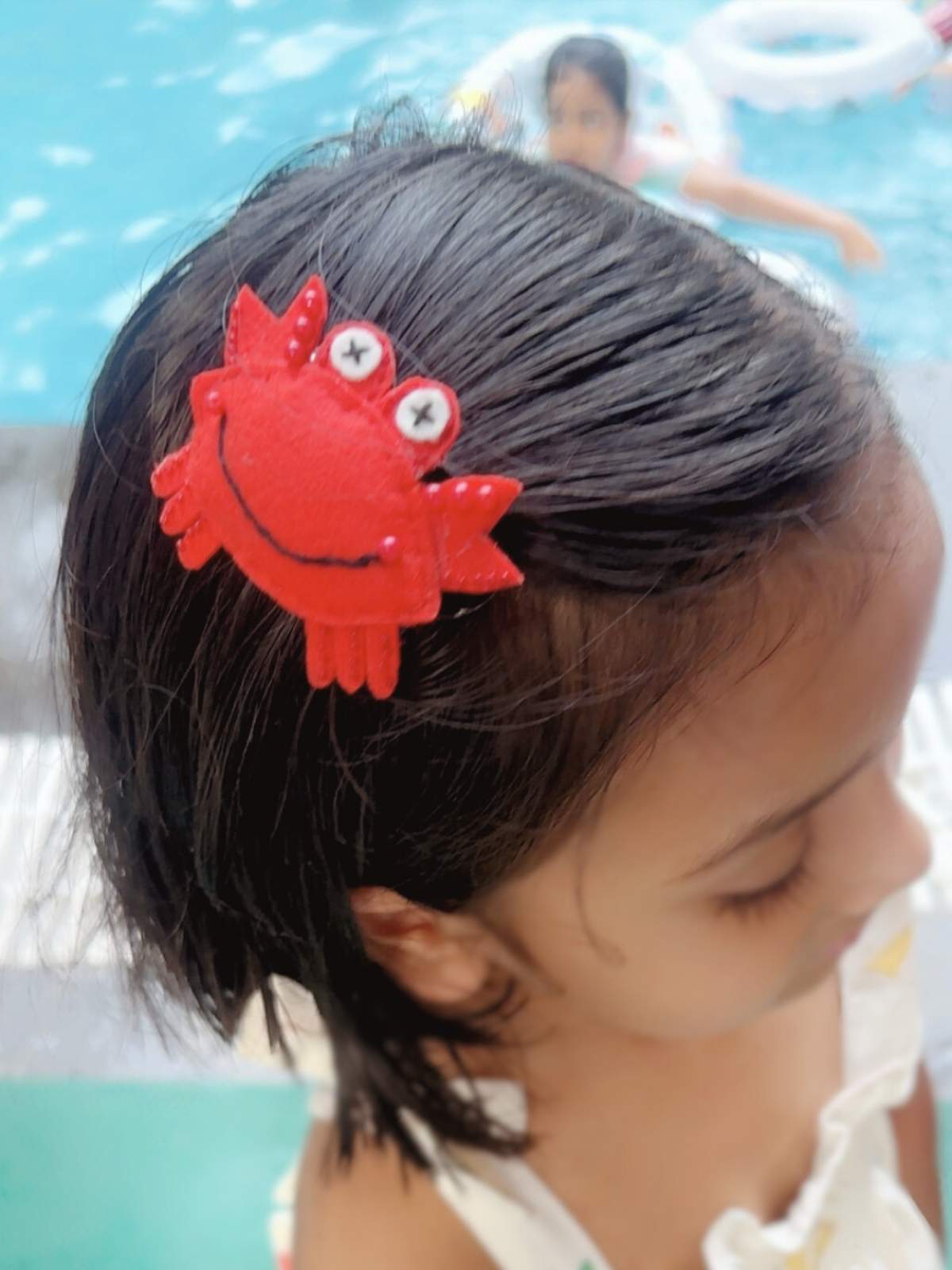 Child with a red crab-shaped hair clip by a pool
