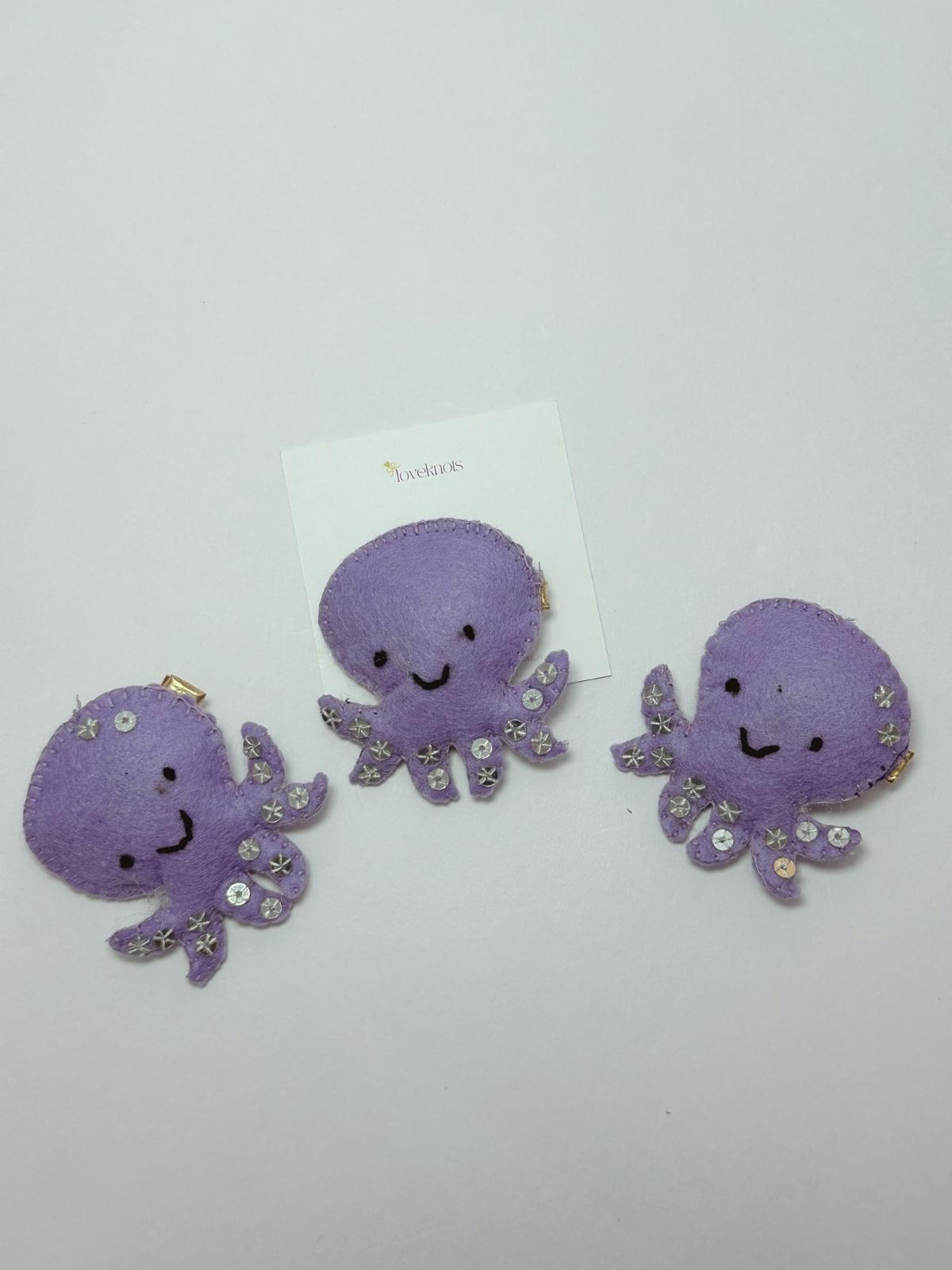  three purple octopus-shaped hair accessories on a white background
