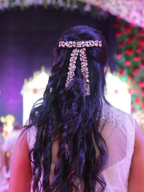 loveknots founder Srishti bansal with long, wavy hair wearing a decorative crystal hair bow by loveknots against a festive background
