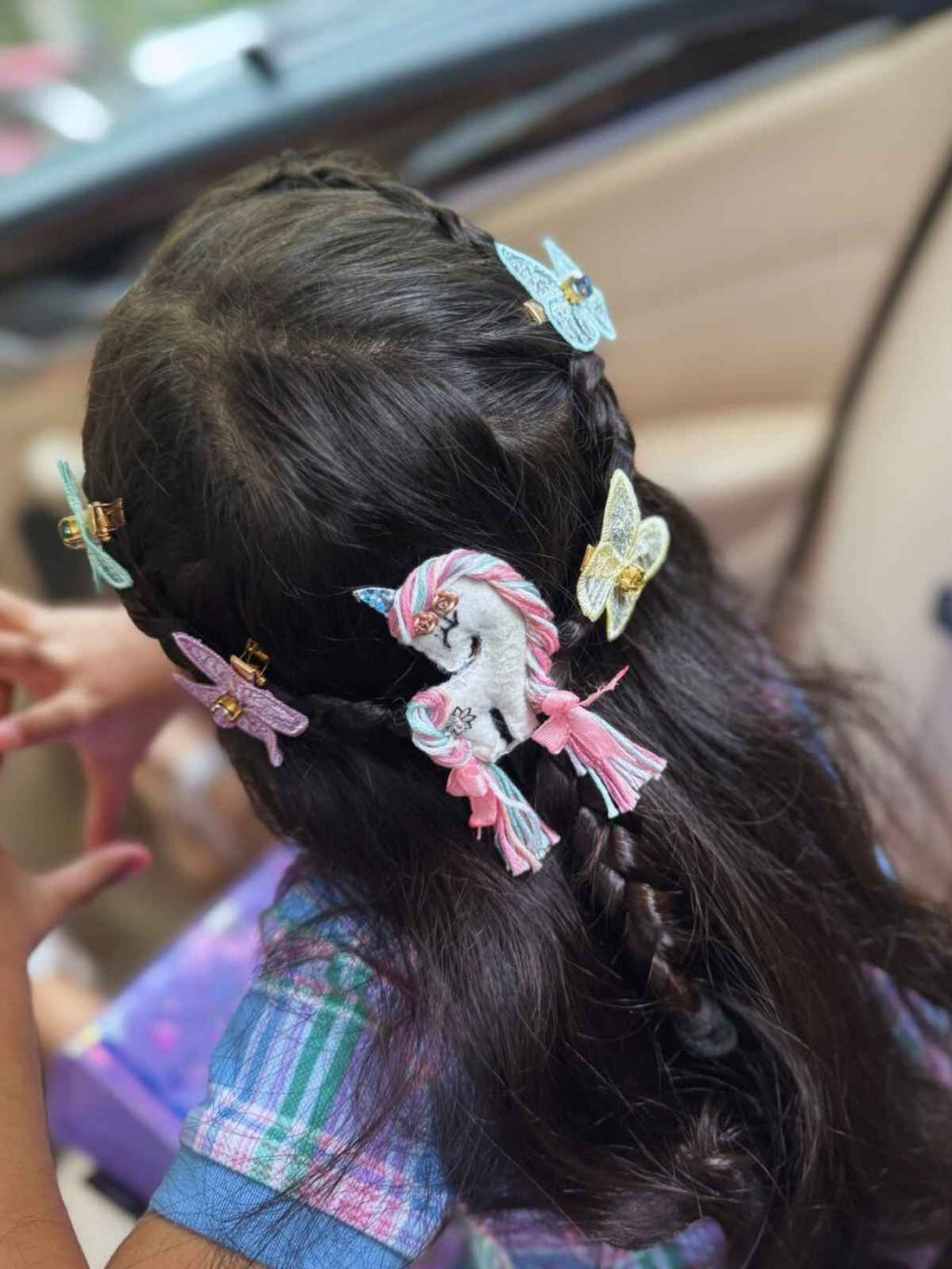 Close-up of a child's hair with unicorn bliss and butterfly clips, sitting in a car.