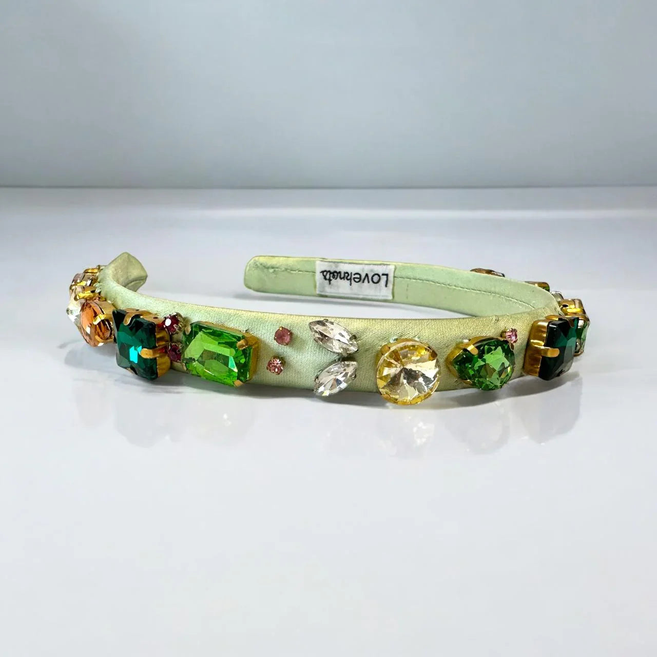 Decorative green headband with colorful gemstones on a white background