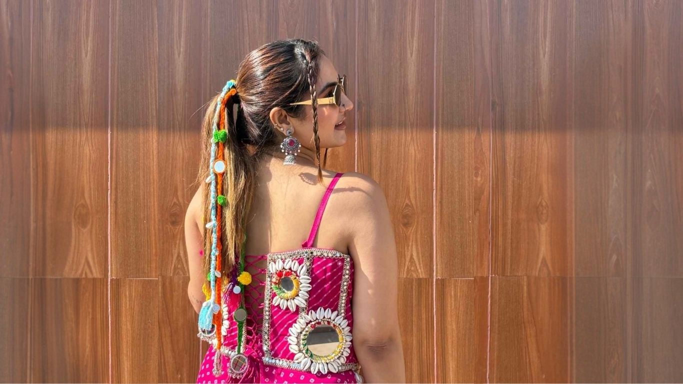 Woman wearing a pink traditional outfit and parandi with floral patterns against a wooden wall.