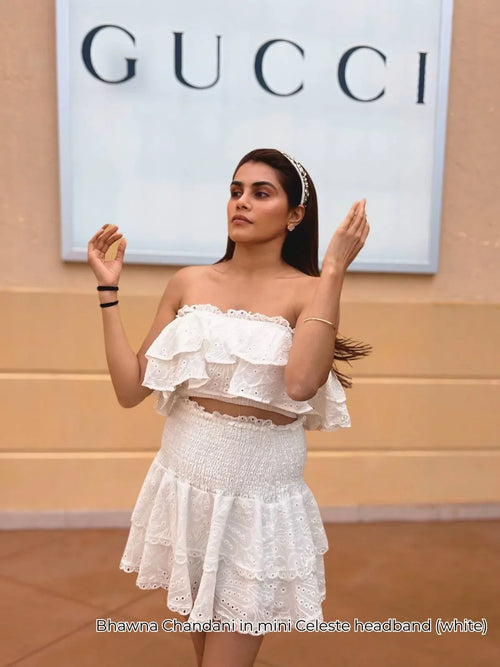Woman wearing a white mini Celeste headband and white ruffled outfit, standing outdoors.