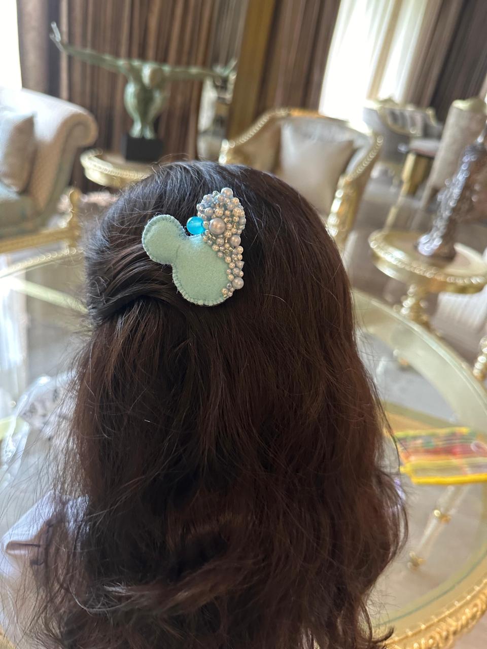 Mickey Mouse shaped hair clip with pearls and a blue gem in a luxurious room
