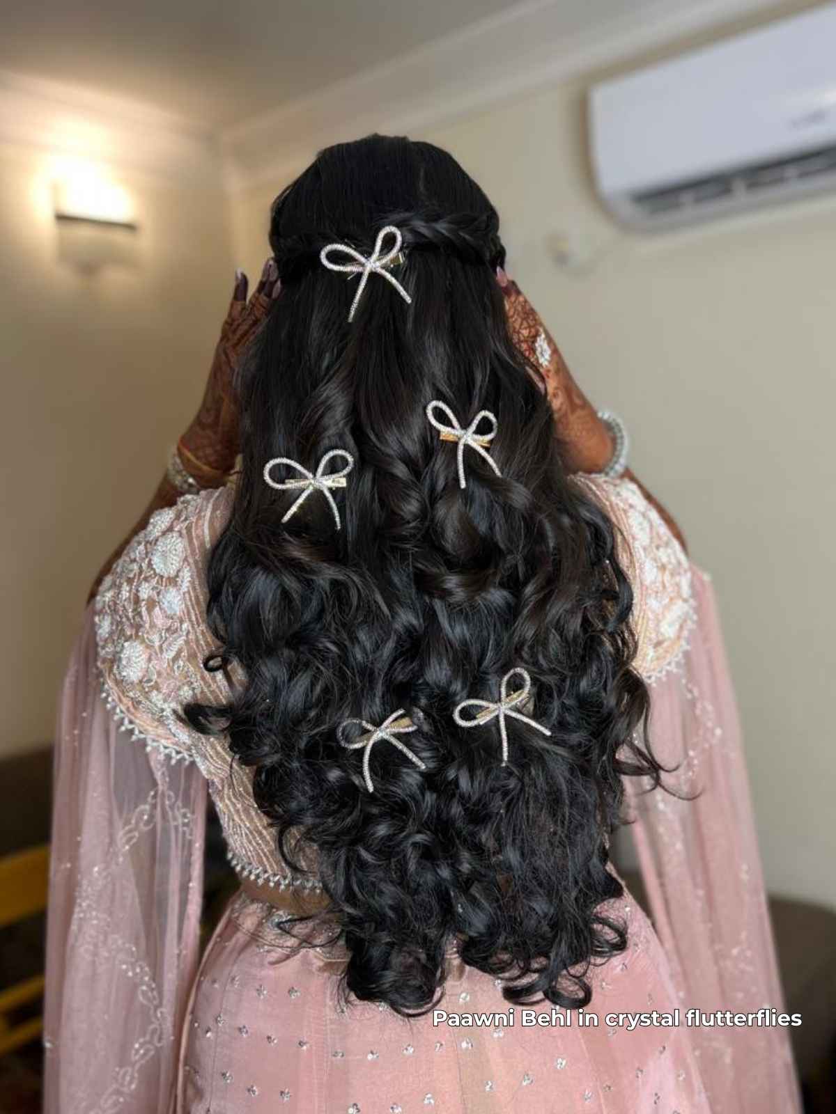 pawn behl with long, wavy hair styled with crystal bows, wearing a pink and gold traditional outfit.