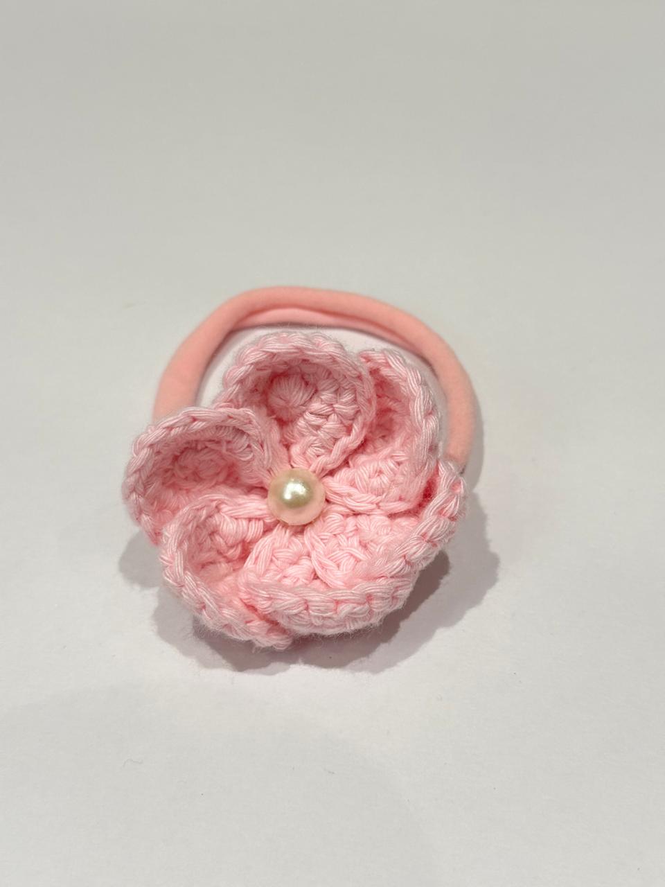 Pink crocheted flower hair tie on a light gray background