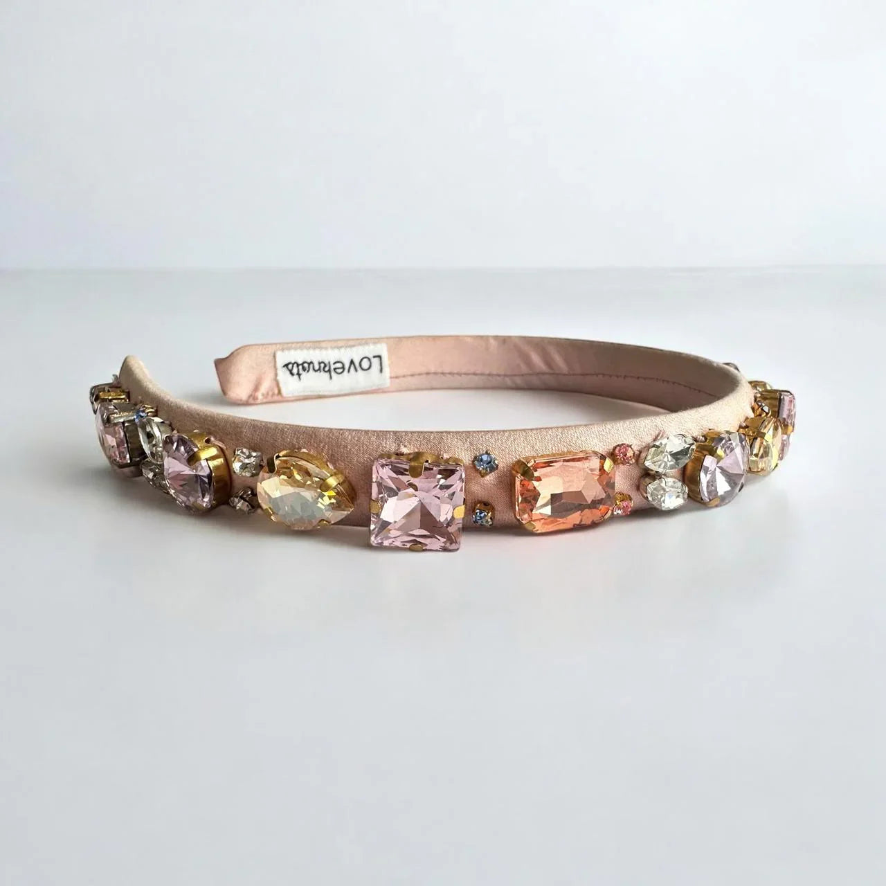 Decorative pink headband with colorful gemstones on a white background