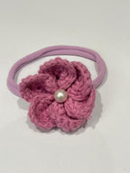 Purple crocheted flower hair tie with a pearl on a white background
