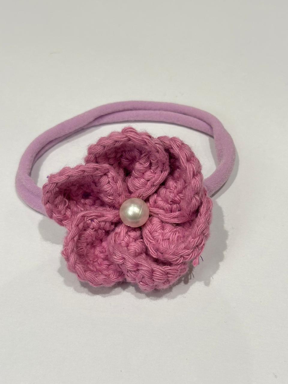 Purple crocheted flower hair tie with a pearl on a white background