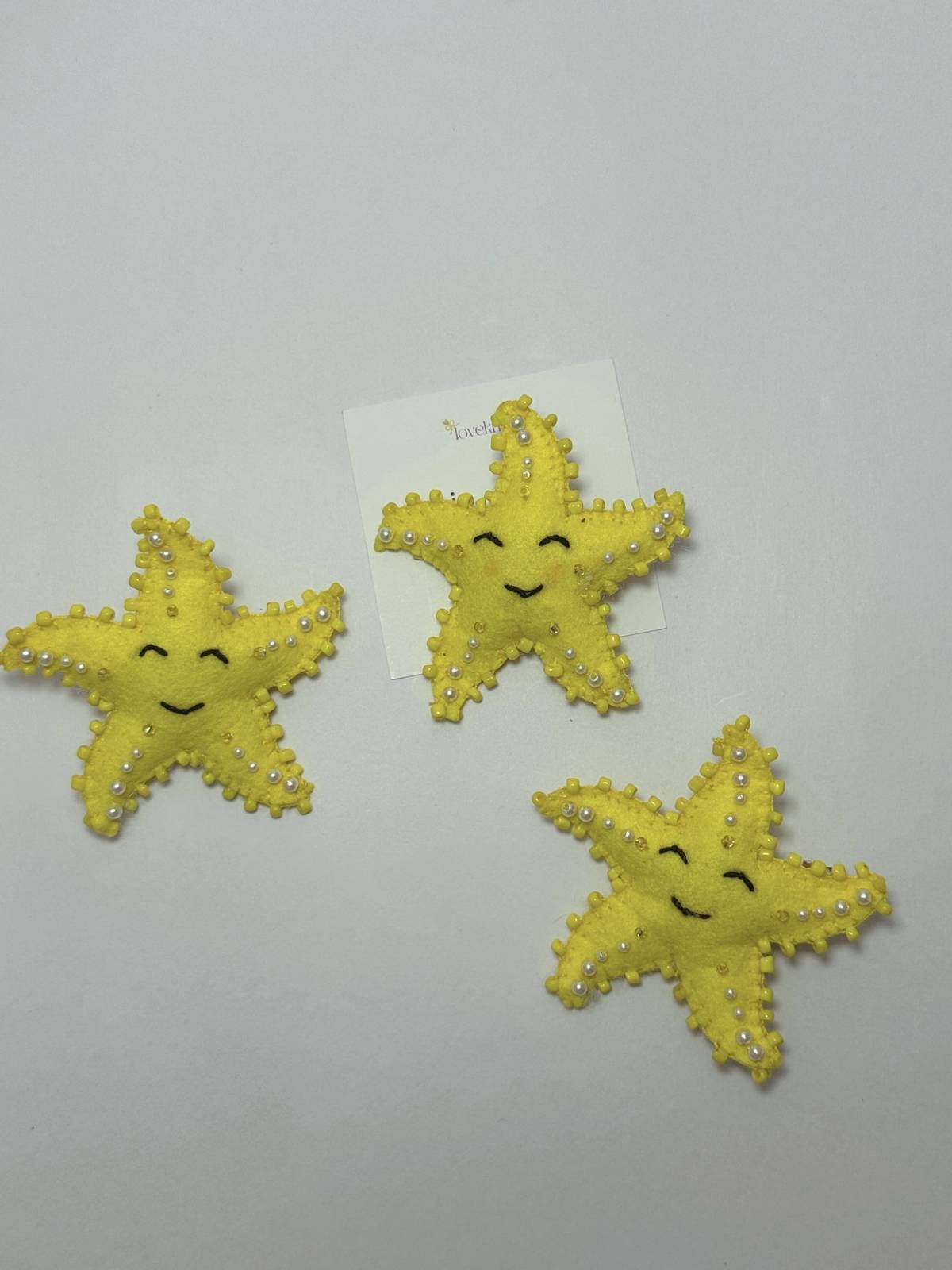 Three yellow star-shaped hair clips with pearl embellishments on a loveknots 