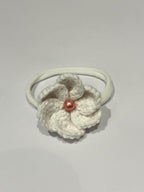 White crocheted flower hair tie with a red bead on a light gray background