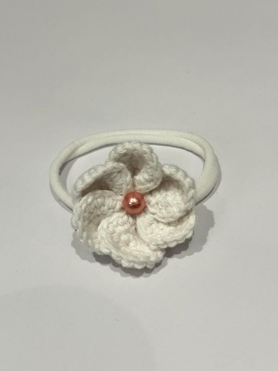 White crocheted flower hair tie with a red bead on a light gray background