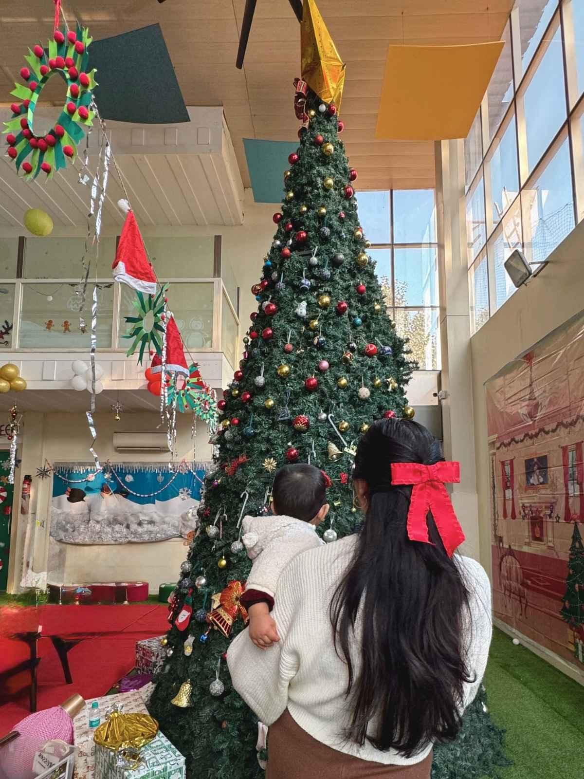 Women wesring red christmas oversized bow standing in front of decorated christmas tree with baby