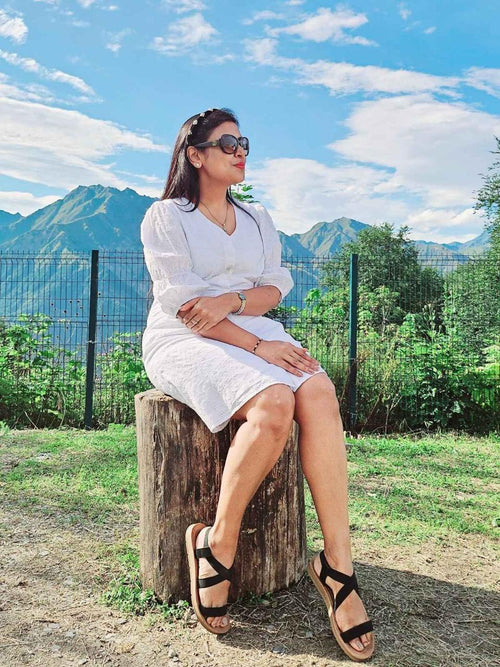Woman in a white dress sitting on a log with mountains in the background wearing loveknots hairband