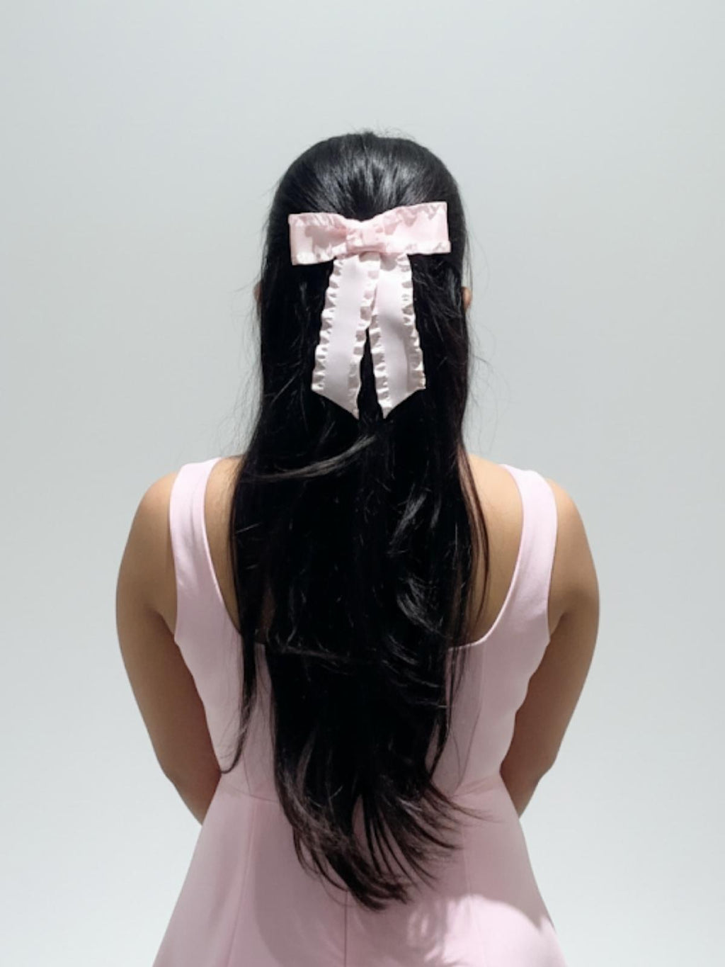 Person with long black hair wearing a pink bow, against a plain background