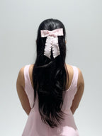 Person with long black hair wearing a pink bow, against a plain background