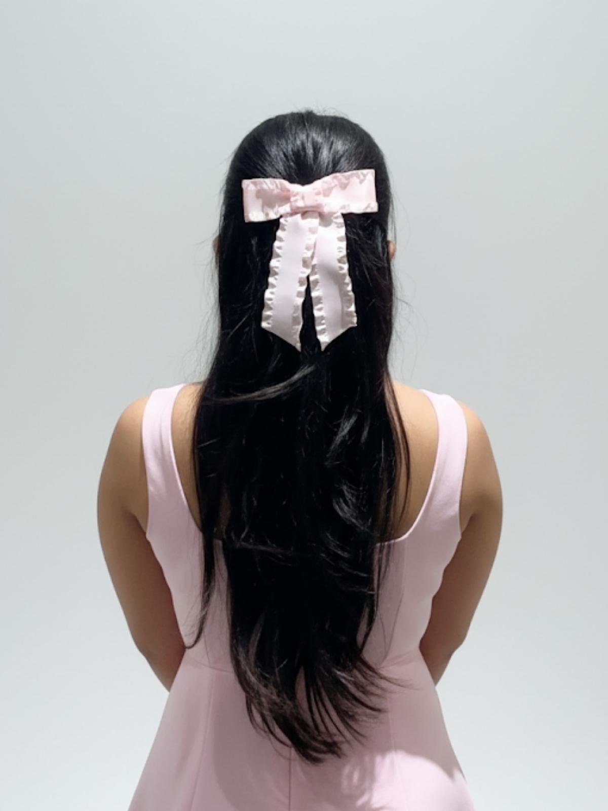 Person with long black hair wearing a pink bow, against a plain background