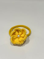 Yellow crocheted flower on a rubber band with a pearl center against a white background